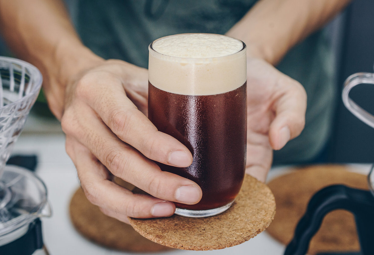 Barista holding and serving a drinking glass of cold brew dip coffee.